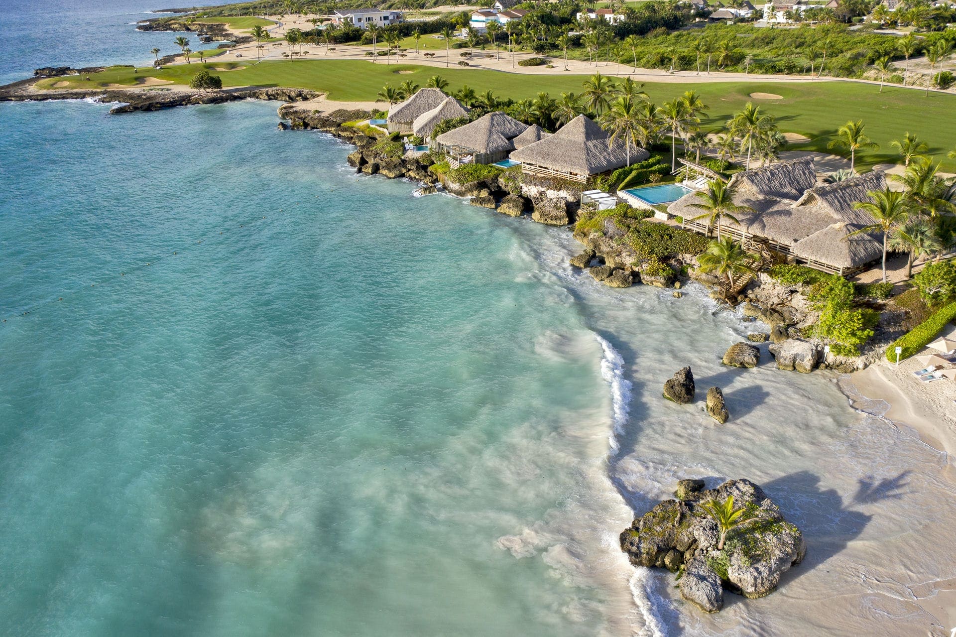 The beach at Caletón, Cap Cana: a sheltered cove of white sand with thatched cabanas above the waterline.